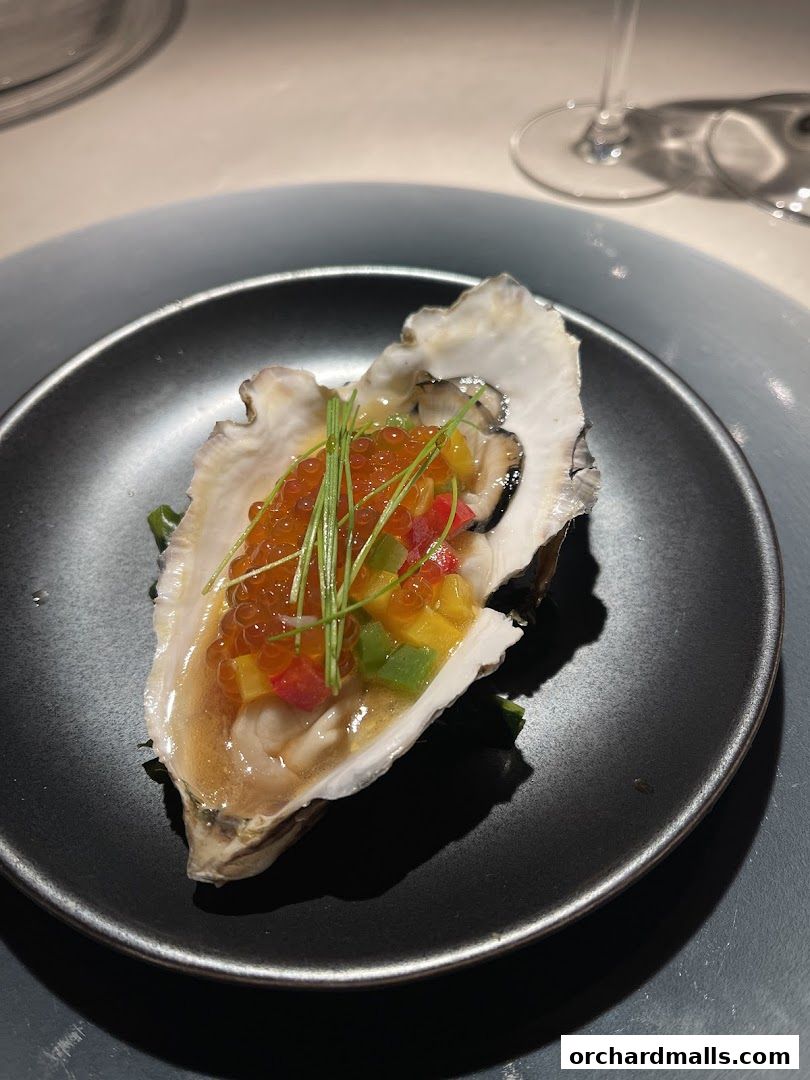 A single oyster topped with roe and diced vegetables on a black plate.