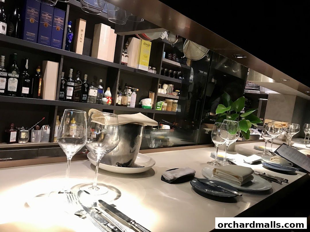 A bar counter set for dining with wine glasses, cutlery, and bottles on shelves.