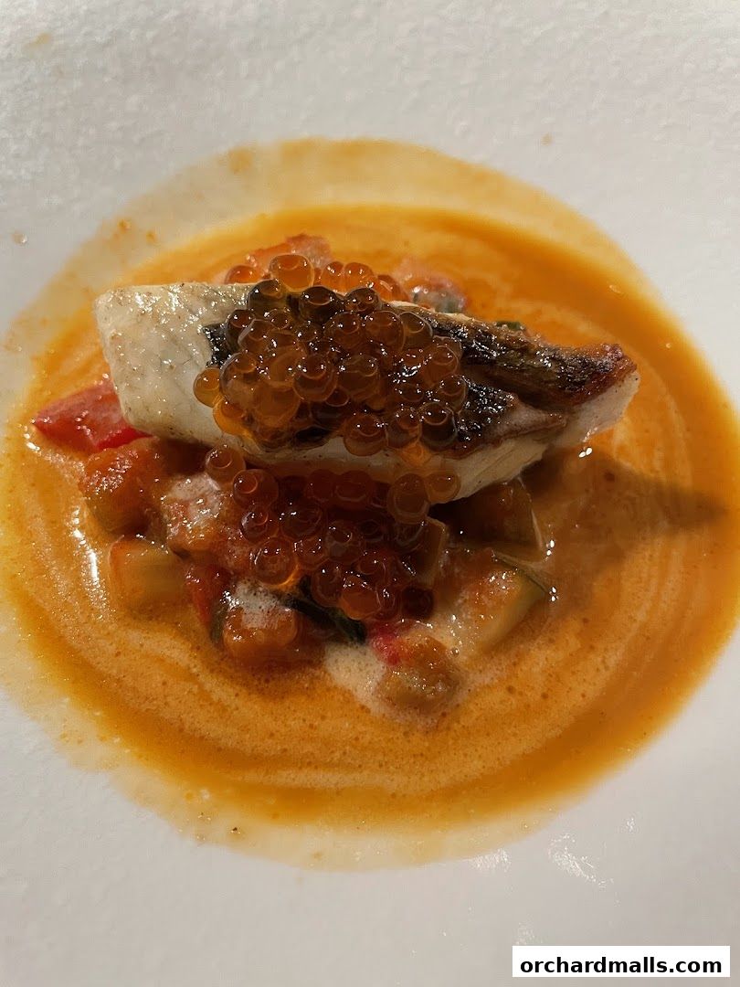 A close-up of a gourmet dish featuring fish, roe, and a rich orange sauce.