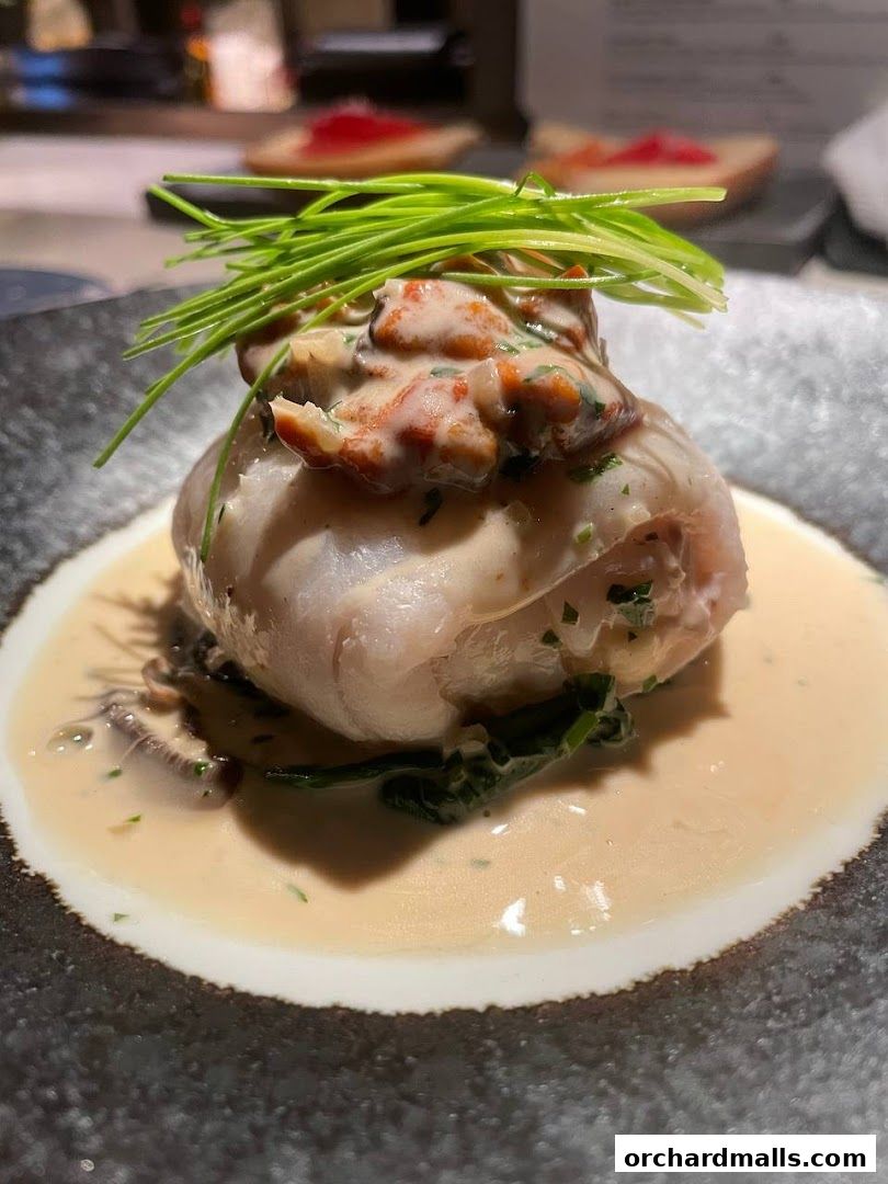 A close-up of a gourmet dish with fish, creamy sauce, and chives.