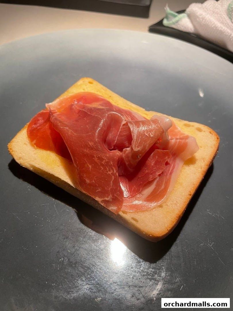 A slice of toasted bread topped with thinly sliced prosciutto.