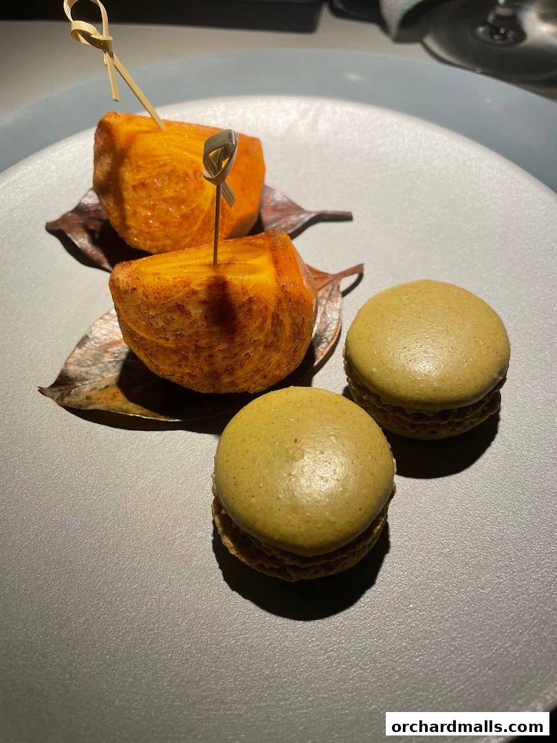 A close-up of two golden-brown fried cubes and two green macarons on a gray plate.