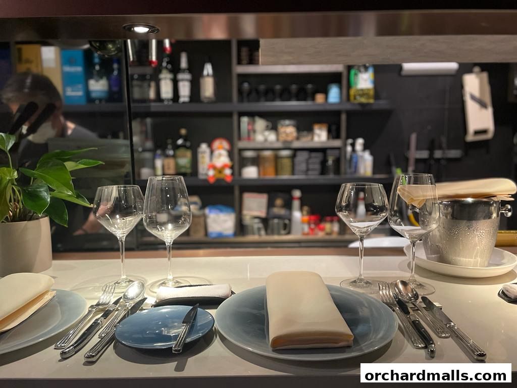 A table setting at Bistro Etroit Ep.2 with wine glasses, cutlery, and a plant.