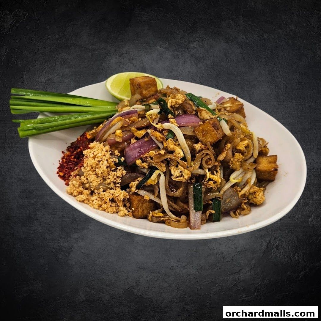 A plate of Pad Thai noodles with tofu, egg, bean sprouts, and lime.