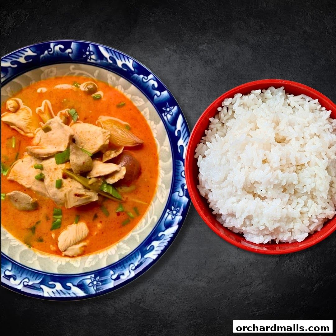 A bowl of Tom Yum soup with chicken and a side of steamed rice.
