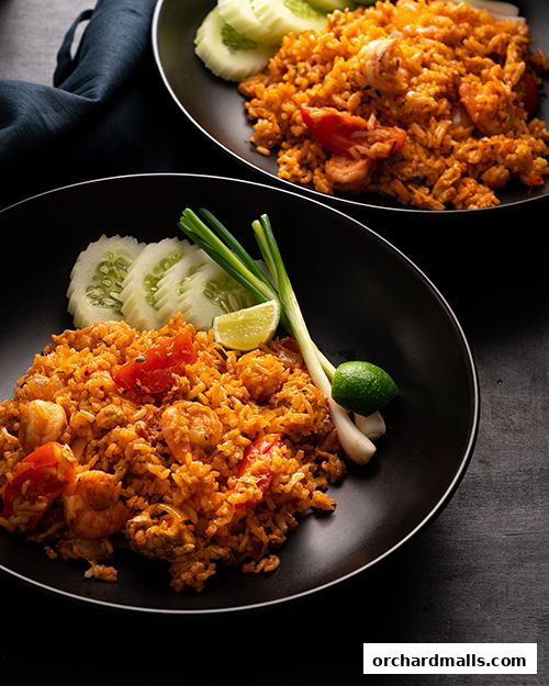 Two plates of delicious Thai fried rice with shrimp, tomatoes, and cucumber garnish.