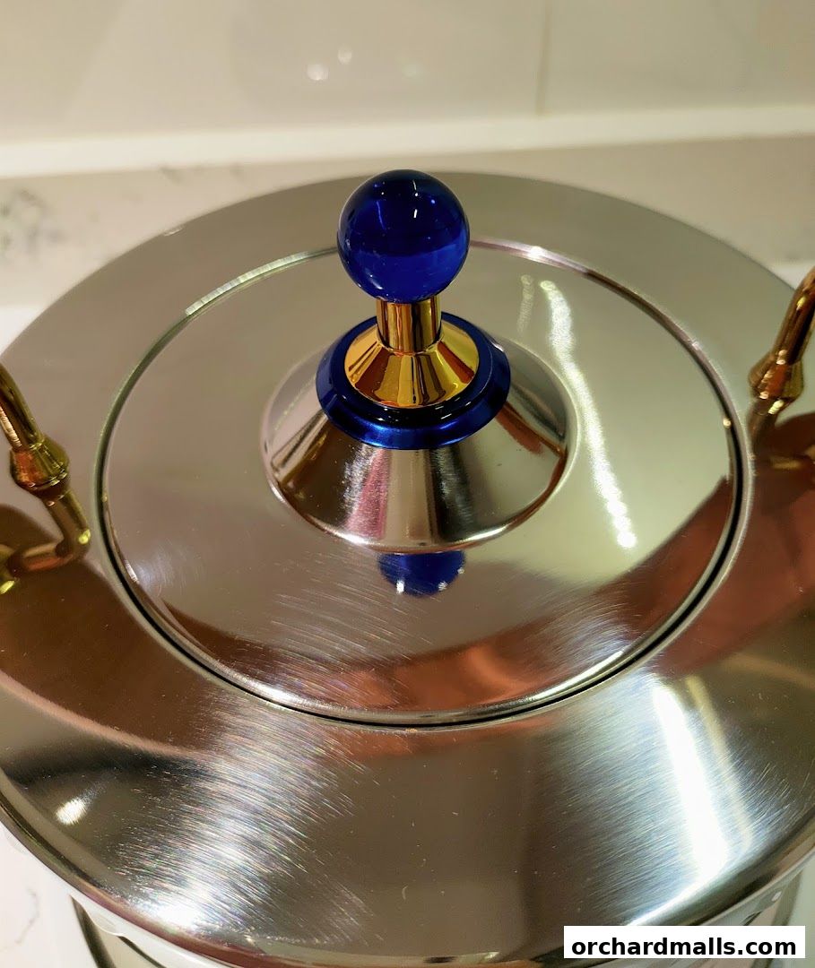 Close-up of a shiny metal teapot with a blue glass knob and gold accents.