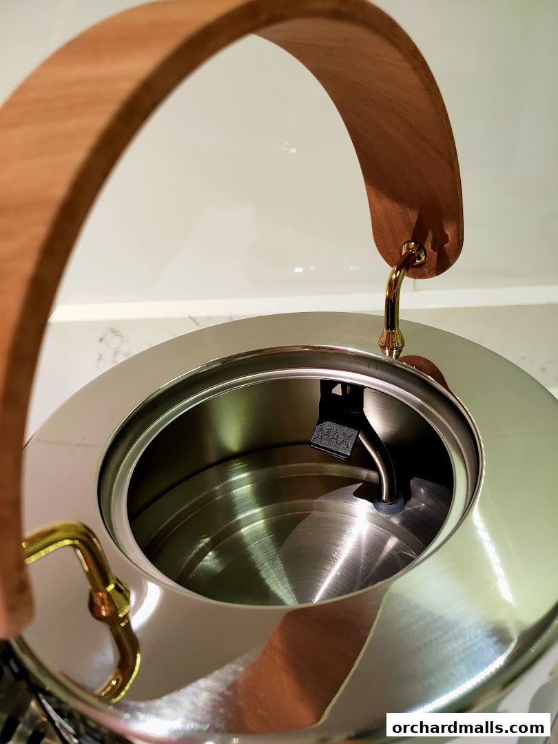 Close-up of a sleek stainless steel kettle with a wooden handle and gold accents.
