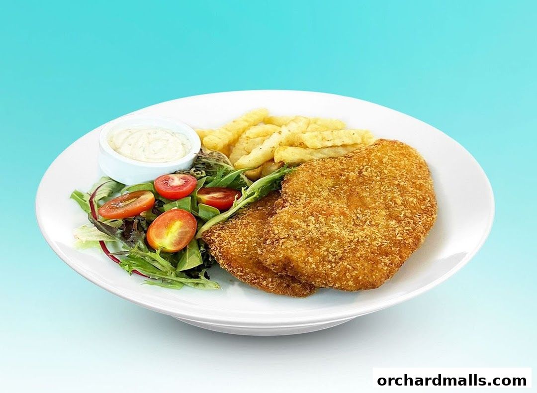 A plate of crispy fried chicken with fries, salad, and dipping sauce.