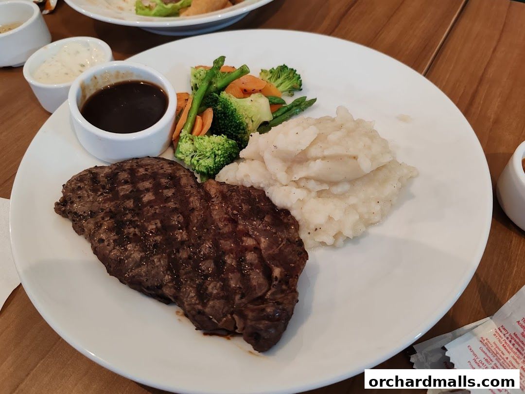 A grilled steak with mashed potatoes and steamed vegetables served on a white plate.