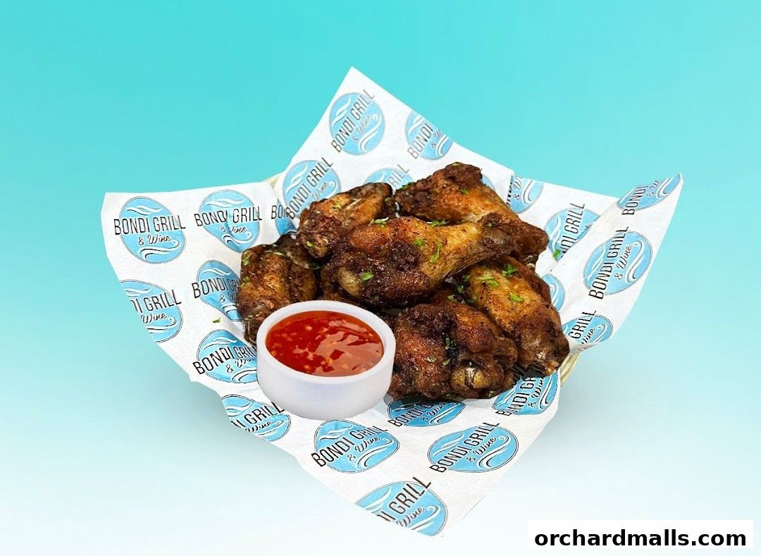 A basket of grilled chicken wings with a side of dipping sauce, served on branded paper.