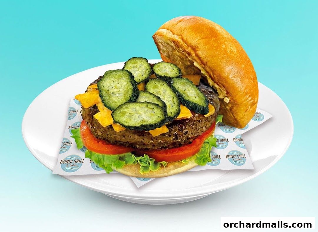 A juicy burger with pickles, cheese, lettuce, and tomato on a white plate.