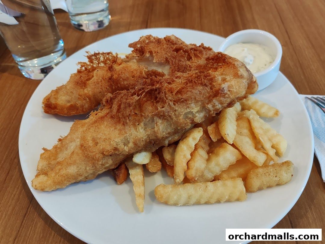 A plate of golden-brown fish and chips with a side of dipping sauce.