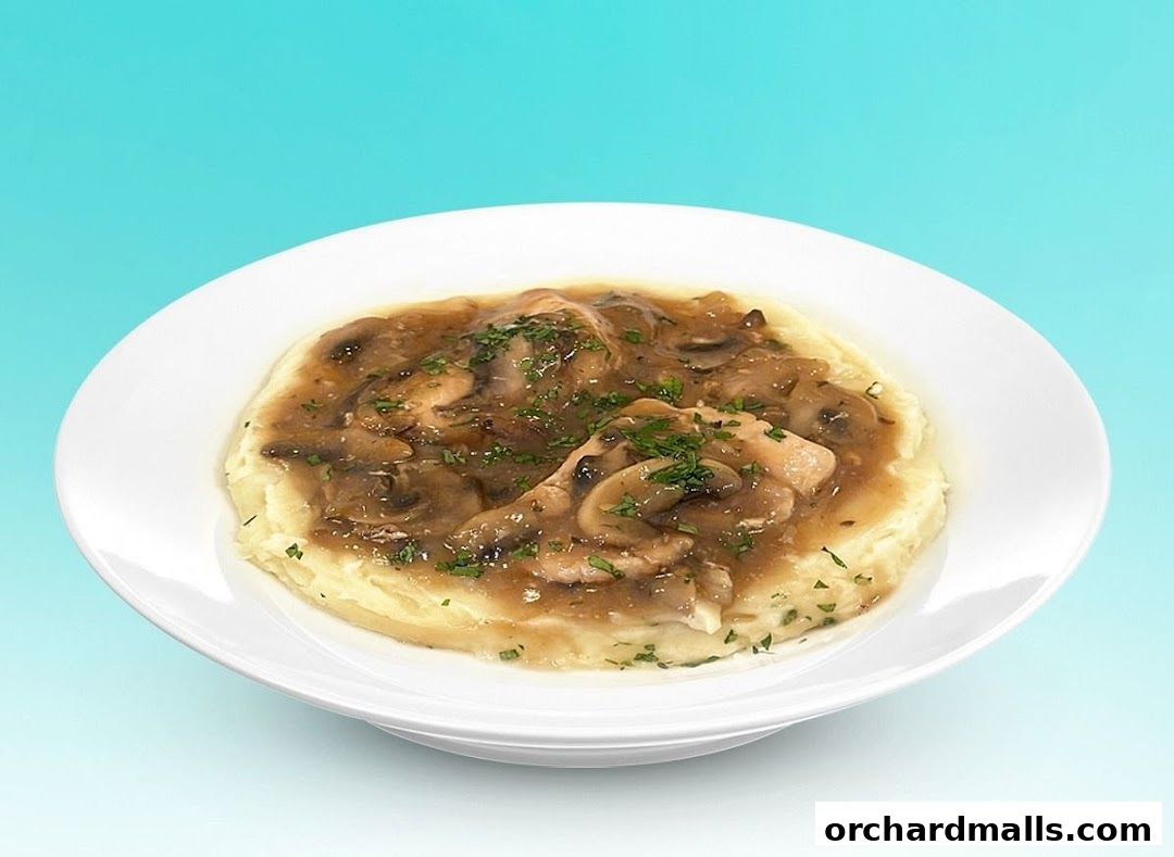 A white bowl filled with mashed potatoes topped with chicken and mushroom gravy.