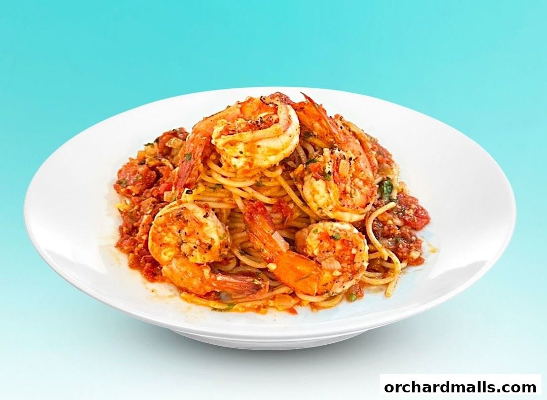 A white plate filled with spaghetti and large shrimp in a tomato-based sauce.