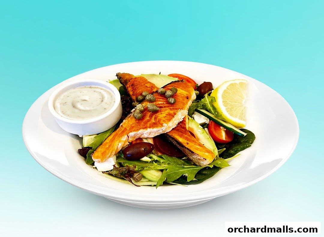 A delicious salmon salad with avocado, tomatoes, olives, and a side of dressing.