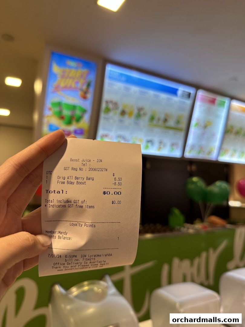 A receipt from Boost Juice ION is held up in front of the shop's illuminated menu boards.