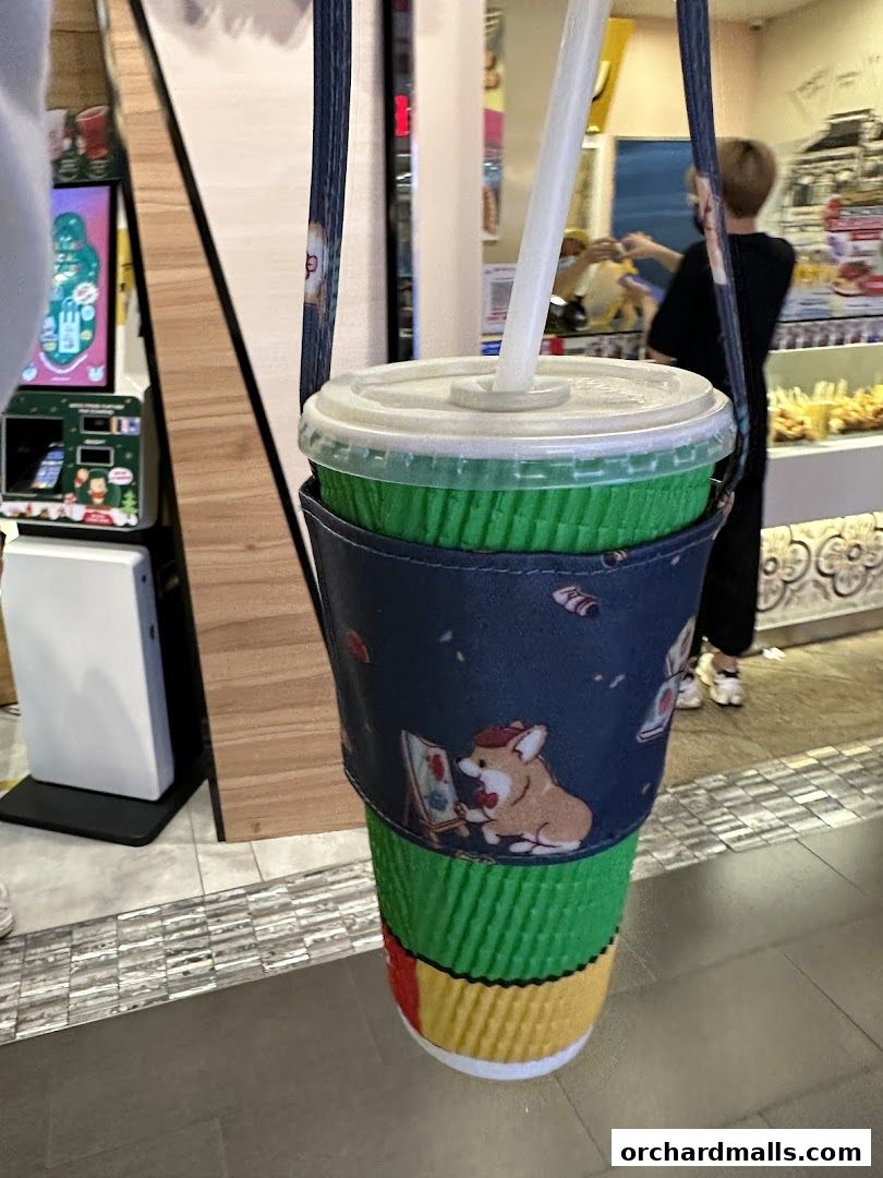 A close-up of a green drink in a cup with a cute corgi sleeve, held by a strap.