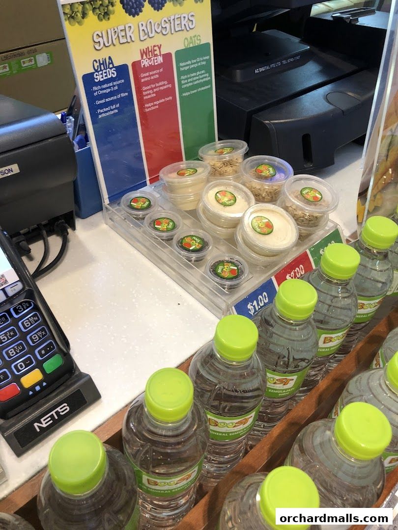 A display of Boost Juice super boosters including chia seeds, whey protein, and oats, with bottled water and a payment terminal.