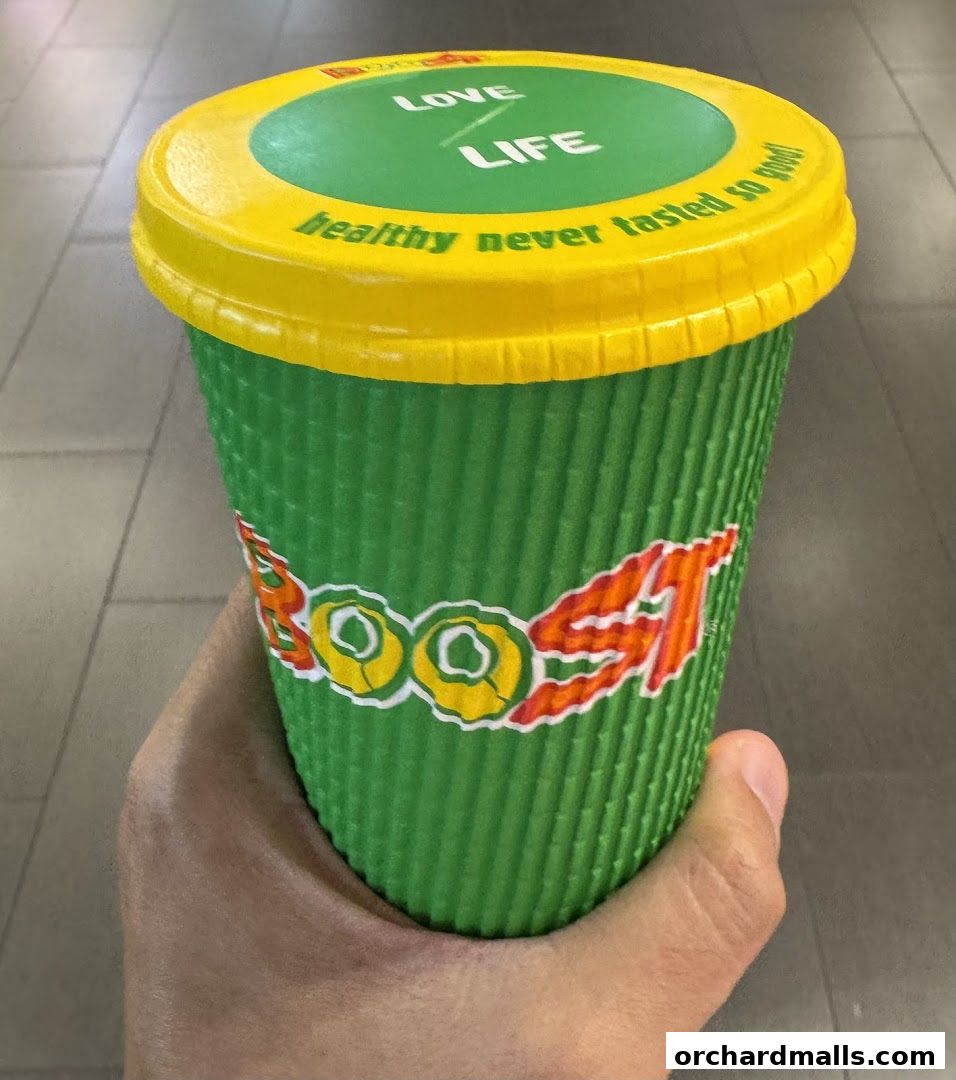A hand holds a green Boost Juice cup with a yellow lid, featuring the brand logo and slogan.