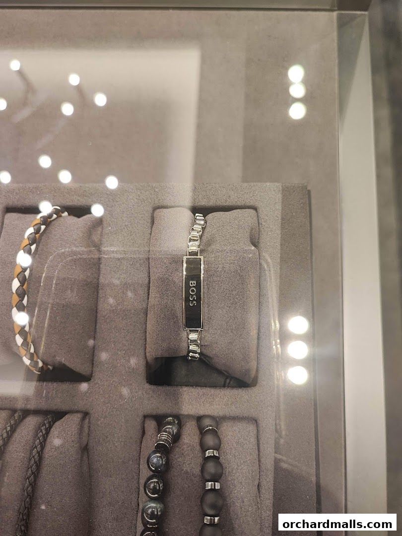 A display case showcasing various BOSS brand bracelets, including a silver chain bracelet with a black plaque.