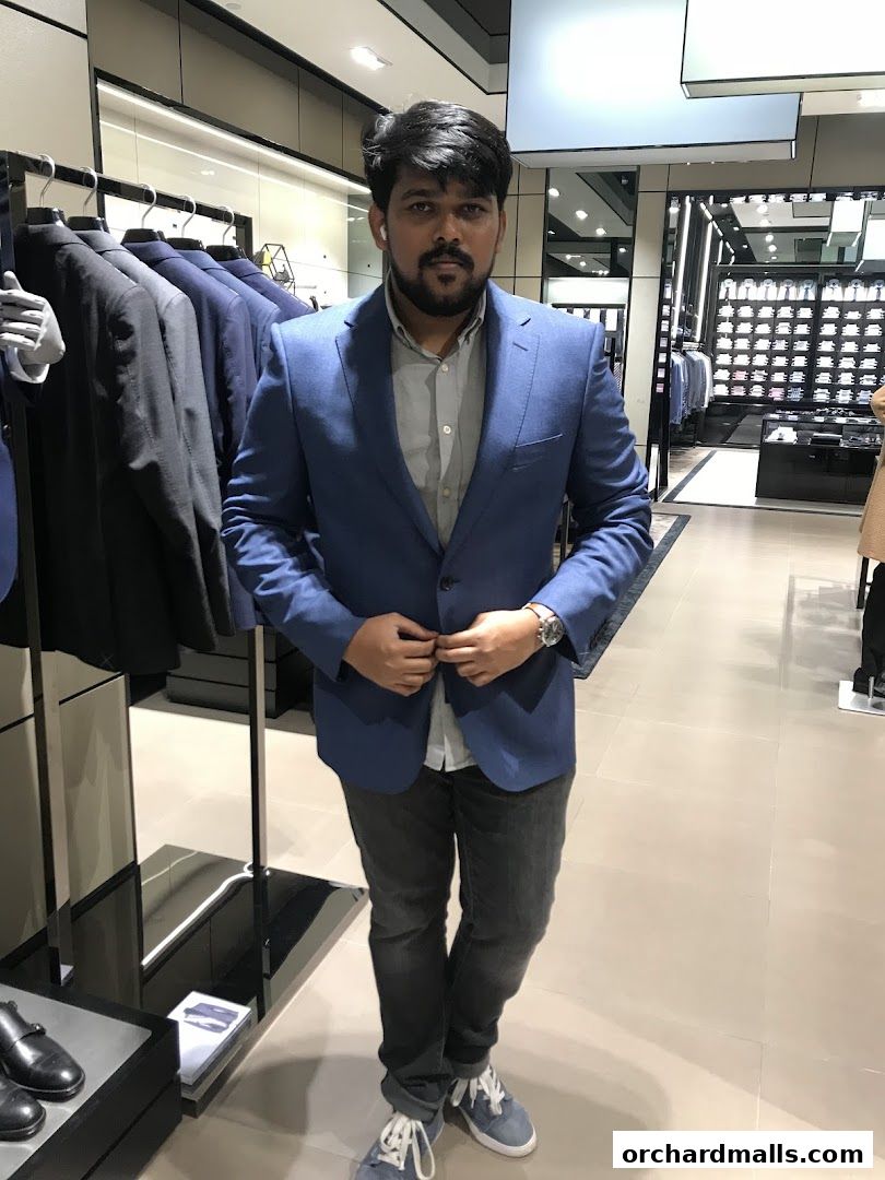 A man in a blue blazer and jeans stands in a BOSS store, surrounded by clothing racks.