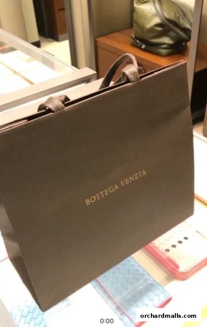 A Bottega Veneta shopping bag with luxury accessories displayed inside a store.