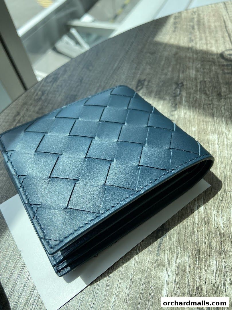 A close-up of a blue Bottega Veneta Intrecciato bi-fold wallet on a wooden surface.