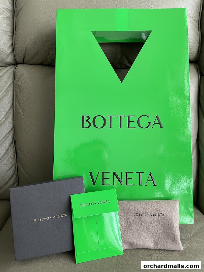 Bottega Veneta shopping bag and packaging on a leather surface.