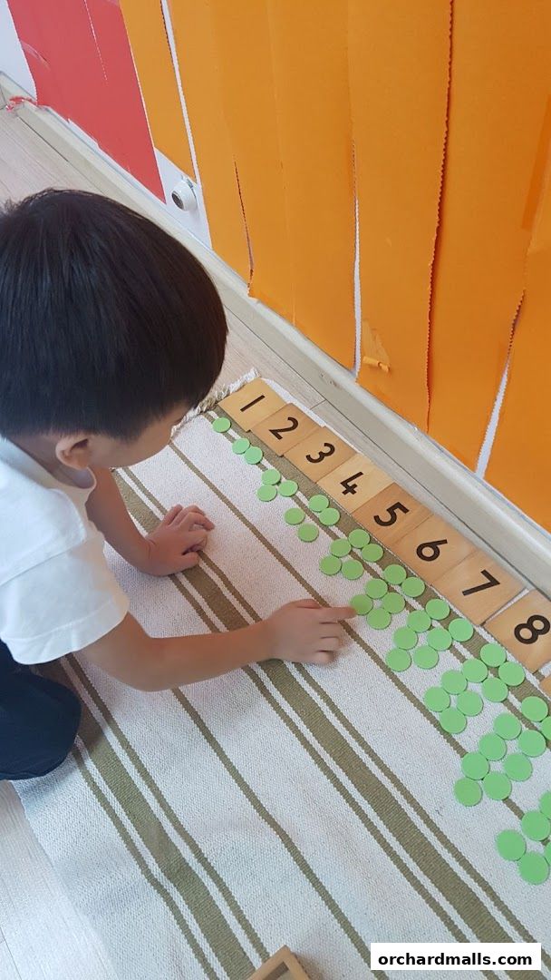 A child learns numbers using Montessori materials with green counters and number tiles.