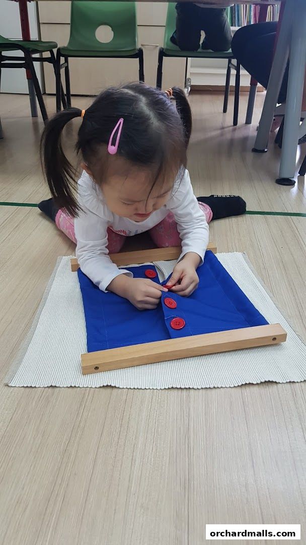 A young child practices buttoning skills on a Montessori dressing frame.