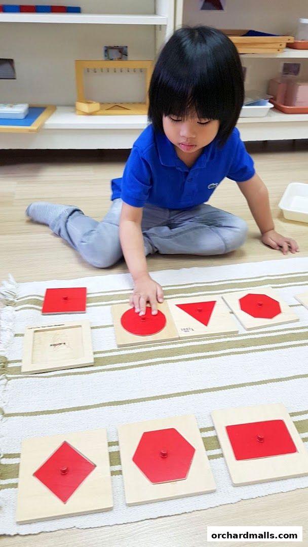 A child learns shapes with Montessori puzzles in a bright, organized classroom.