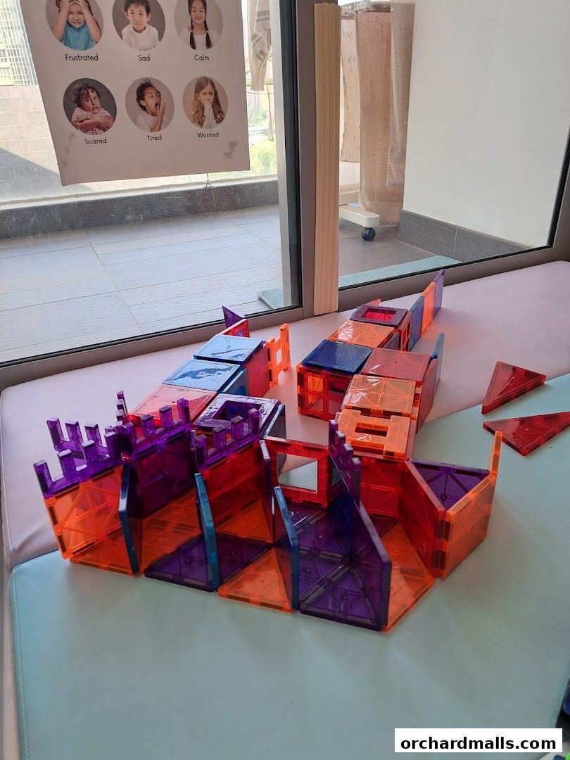 Colorful magnetic building blocks are arranged on a surface, with a poster of children's emotions in the background.