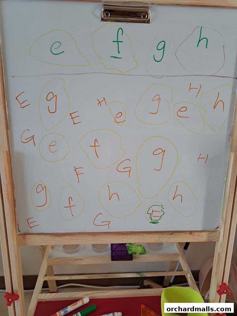 A whiteboard with letters 'e', 'f', 'g', and 'h' written in various colors and sizes.