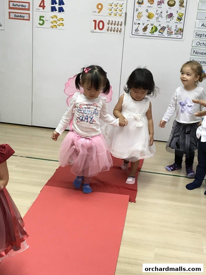 Children in costumes walking on a red carpet at a learning center.