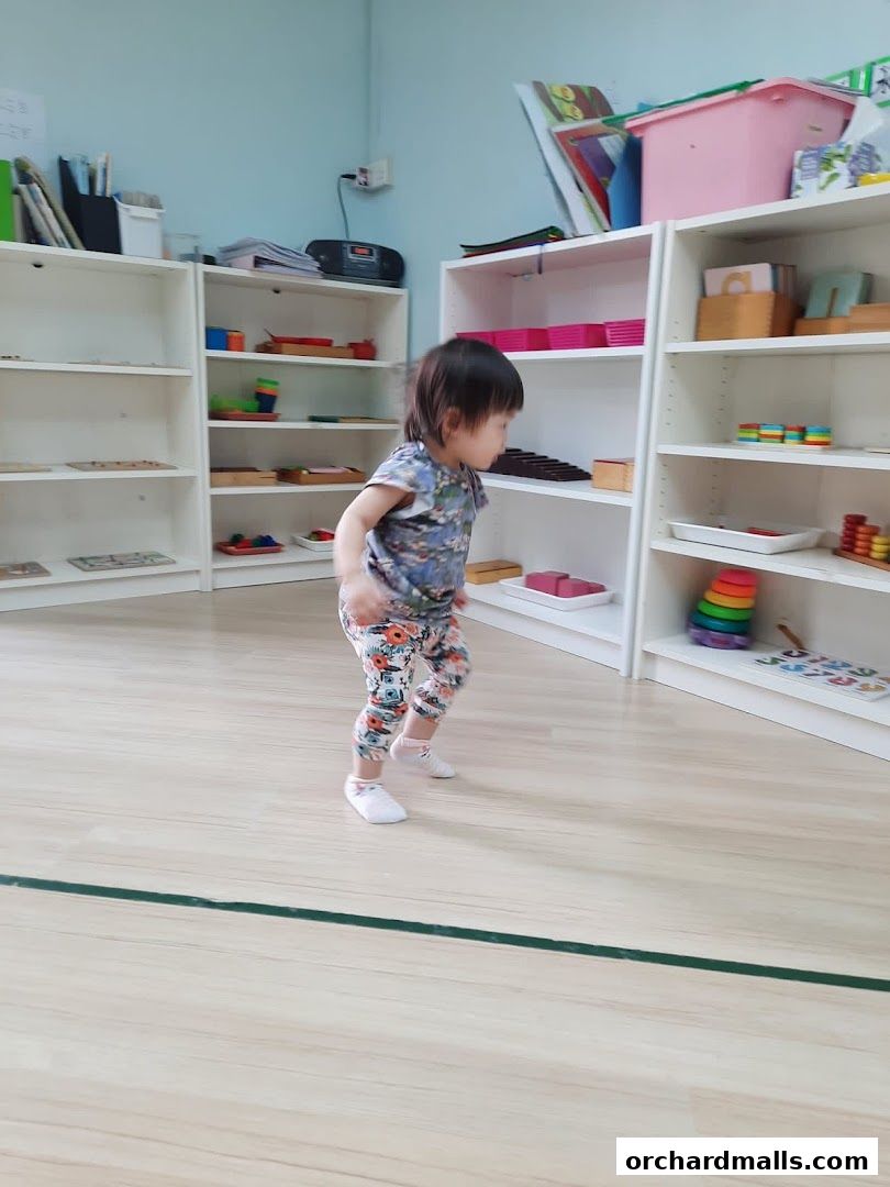 A young child walks through a brightly lit Montessori learning center with shelves of educational materials.