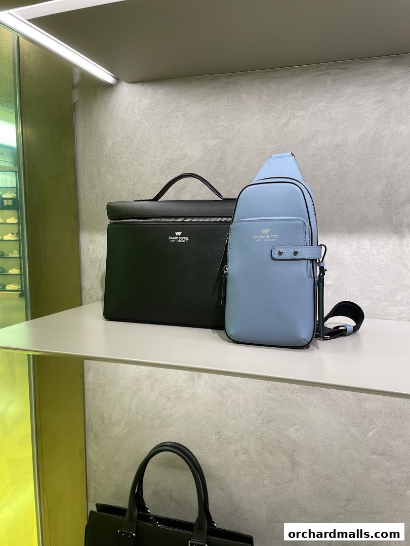 A black briefcase and a light blue sling bag from Braun Büffel are displayed on a shelf.