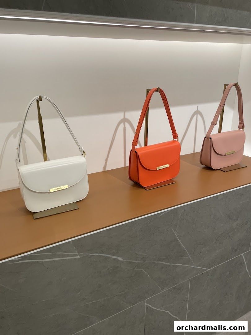 Three stylish handbags in white, orange, and pink displayed on a shelf.