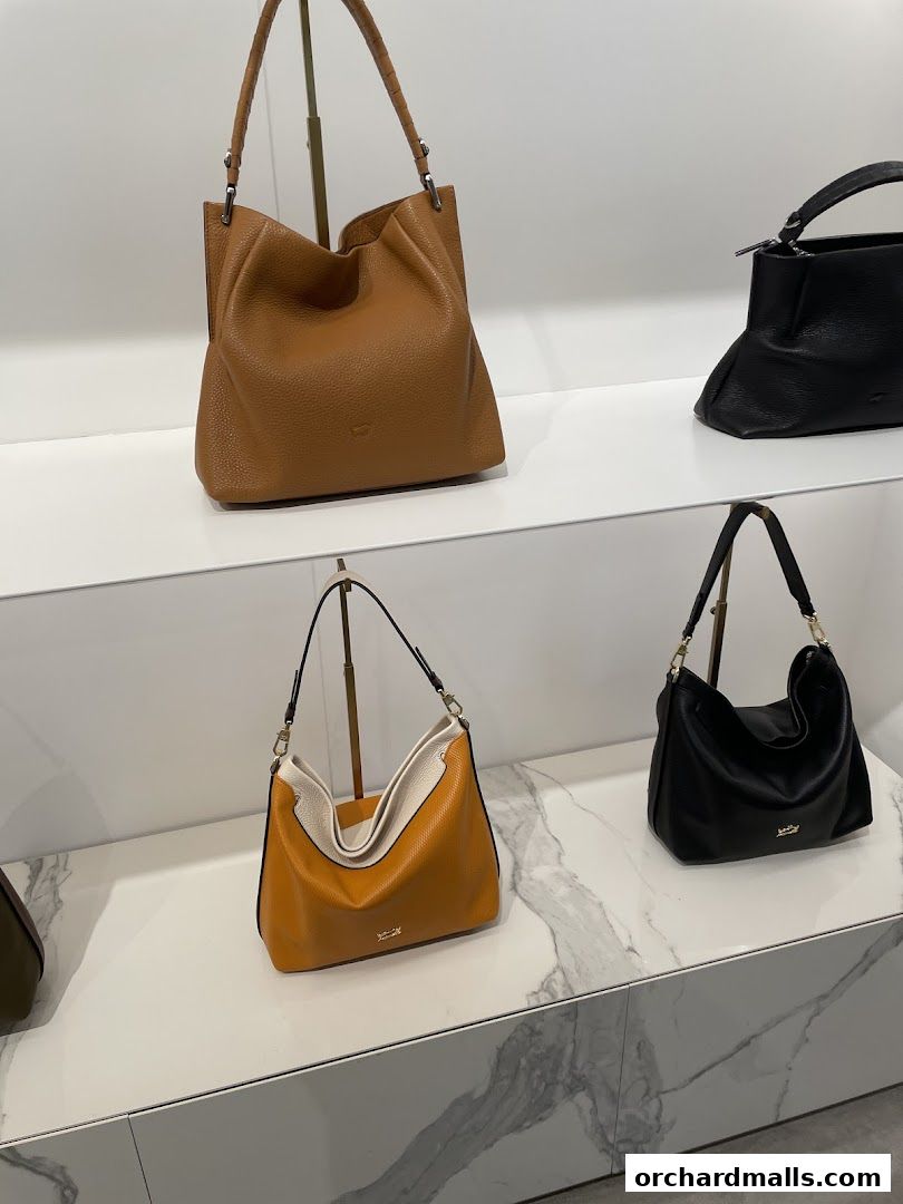 A display of stylish leather handbags in various colors on white shelves.