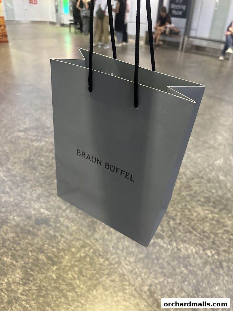 A grey shopping bag with the Braun Büffel logo is held by black ropes.