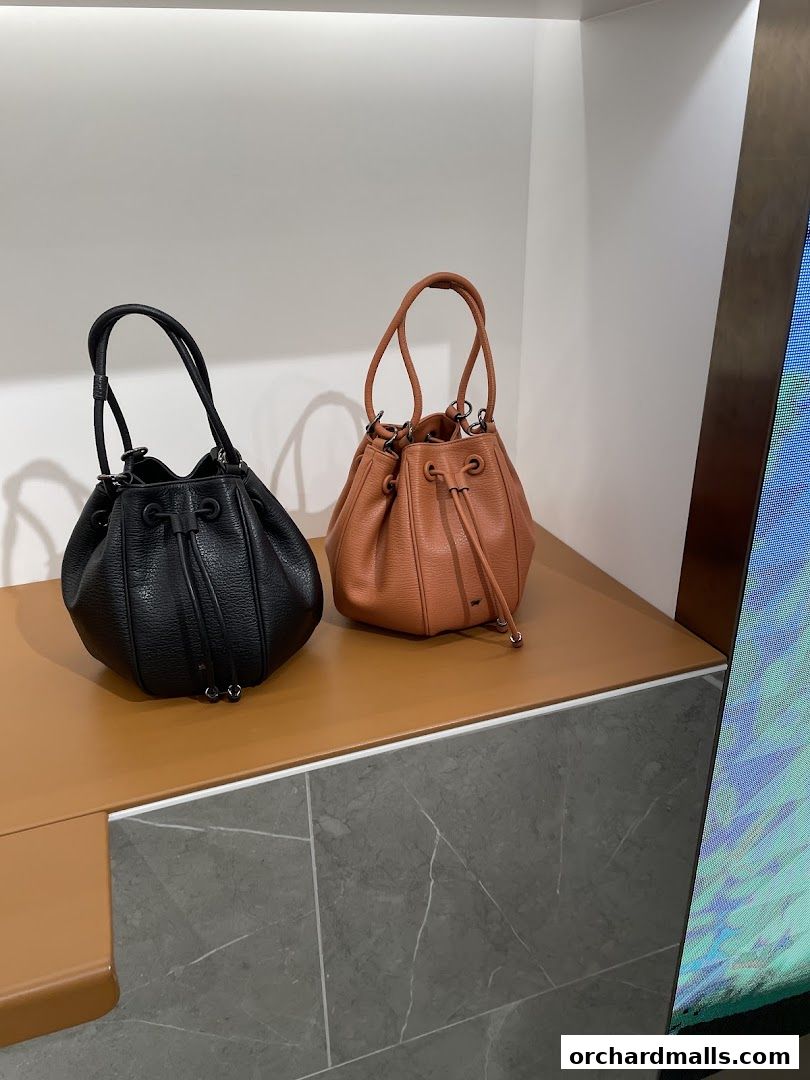 Two textured leather bucket bags, one black and one tan, displayed on a shelf.