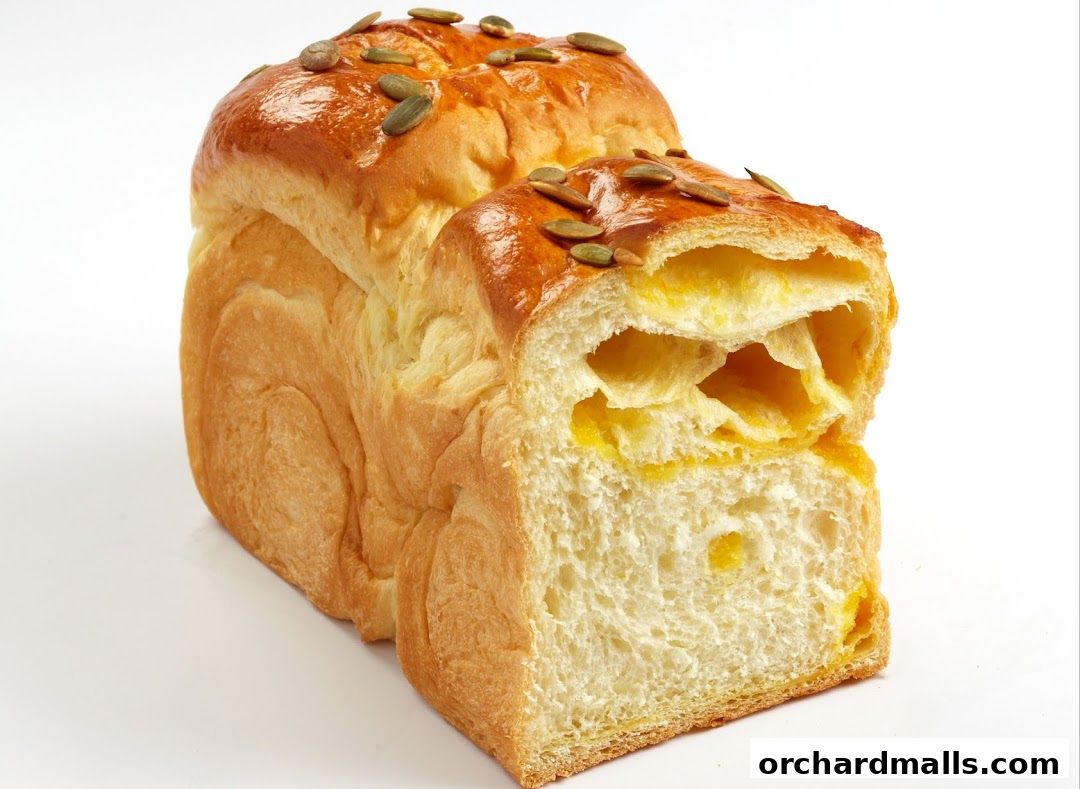 A golden-brown loaf of bread topped with pumpkin seeds, sliced to reveal a soft, fluffy interior.