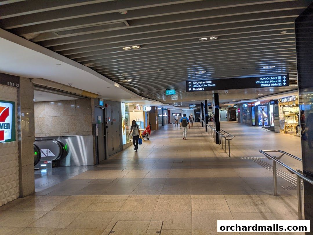 A wide view of a modern shopping mall corridor with people walking and directional signs.