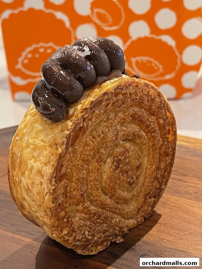 A close-up of a flaky pastry with chocolate frosting and sprinkled sugar.