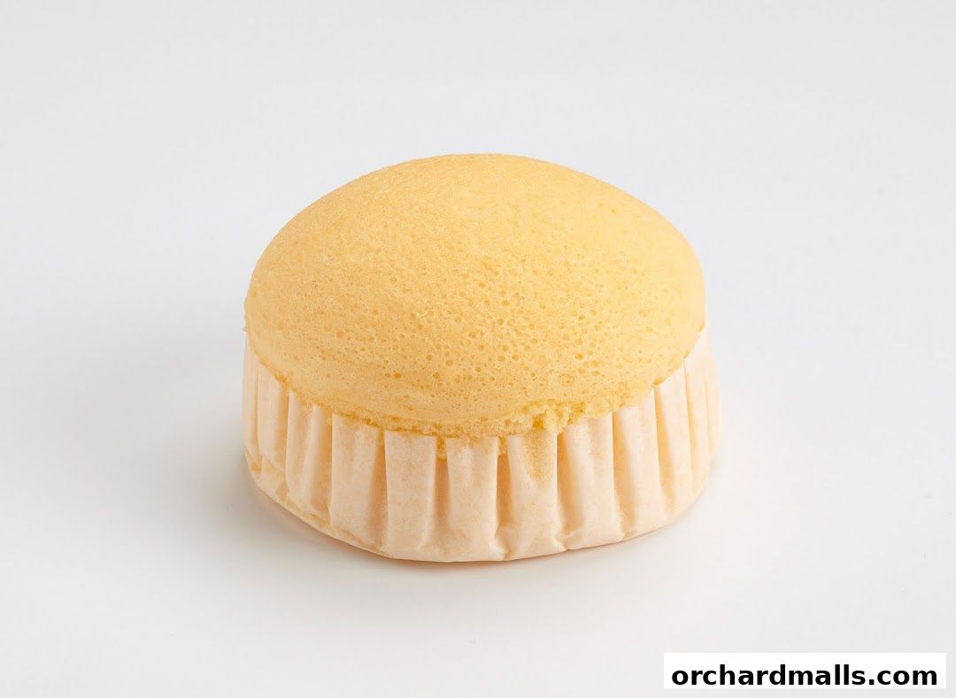 A fluffy, golden-yellow cake with a pleated paper liner sits on a white background.