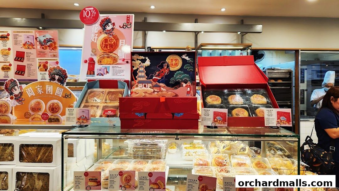 A bakery display featuring mooncakes and other pastries, with promotional materials and staff in the background.