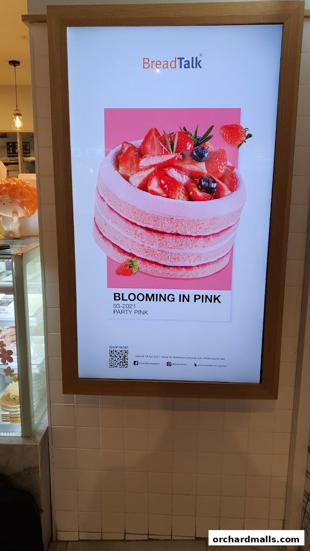 A digital display at BreadTalk showcases a pink cake adorned with strawberries and blueberries.