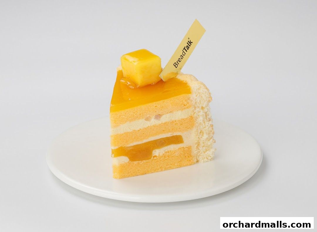 A slice of orange cake with cream and mango filling, topped with a mango cube.