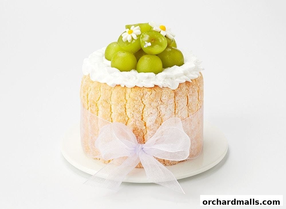 A small, round cake topped with whipped cream, green grapes, and edible flowers.