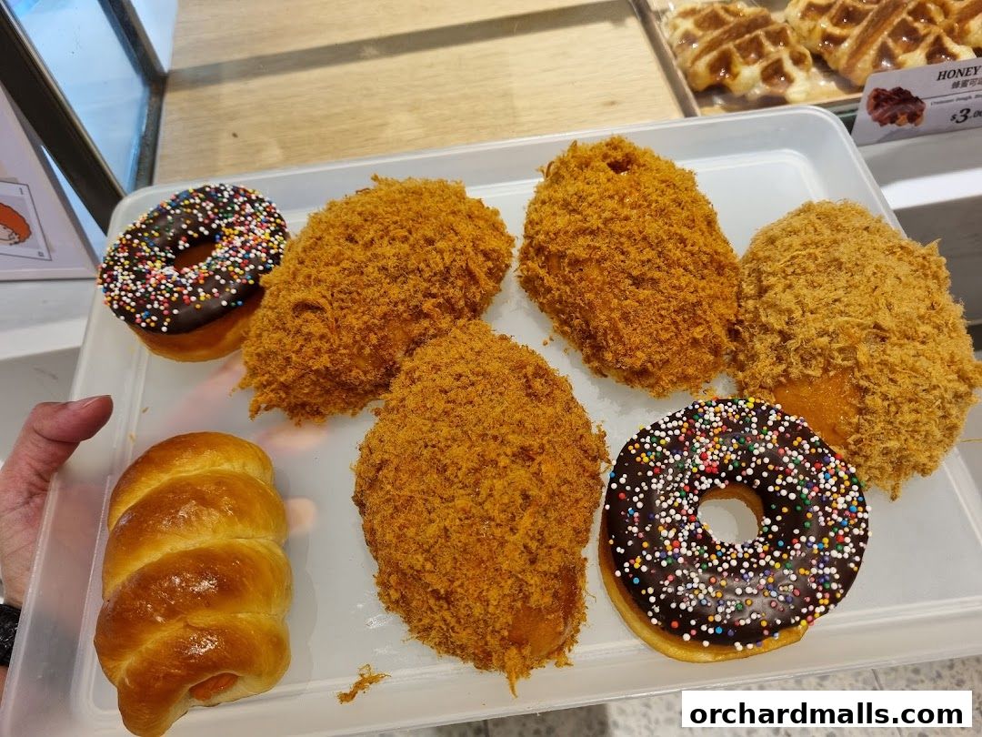 A tray of assorted baked goods including donuts, savory buns, and waffles.